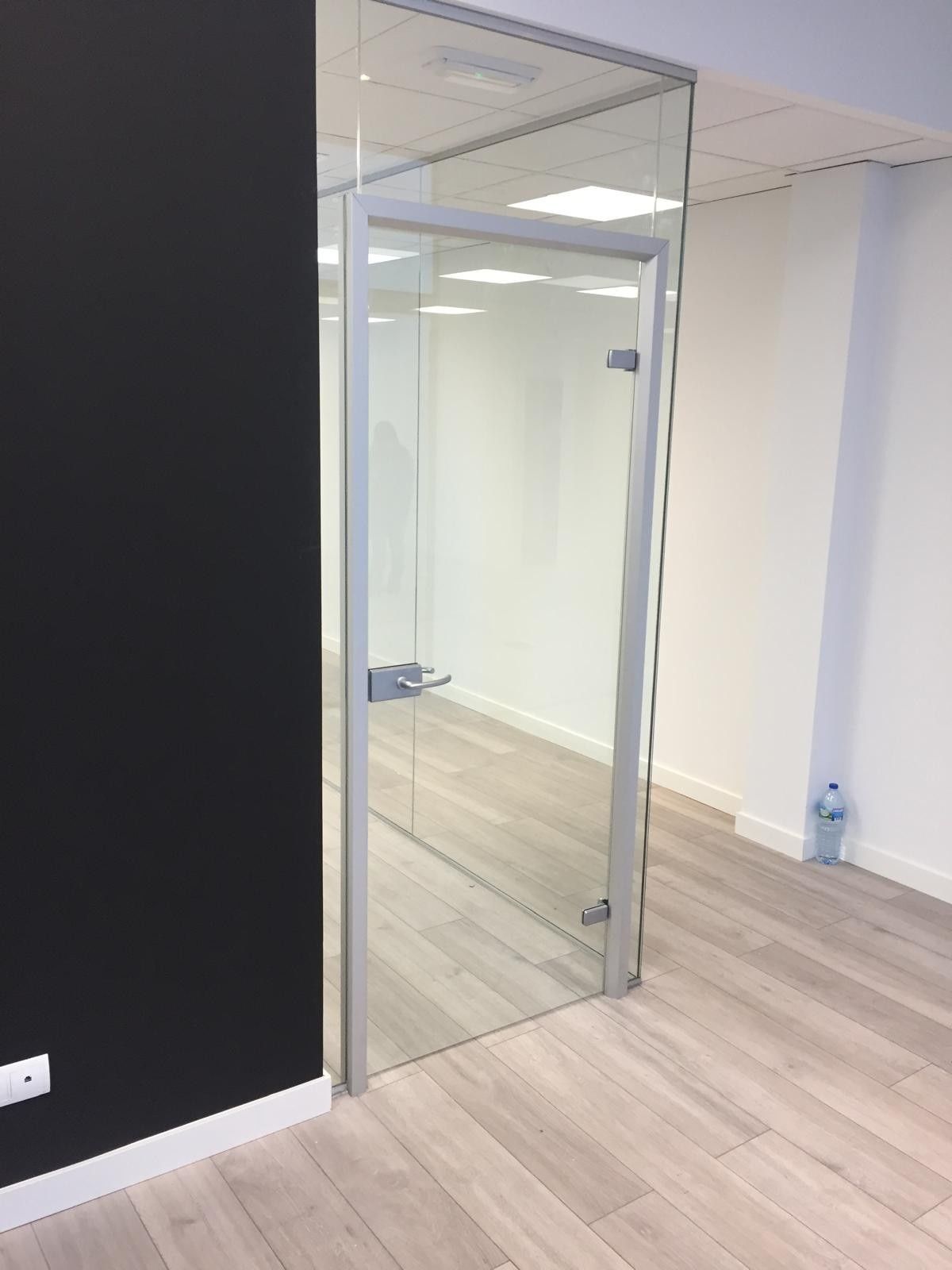 Oficina vacía con puerta de cristal, paredes blancas y suelo de madera clara.