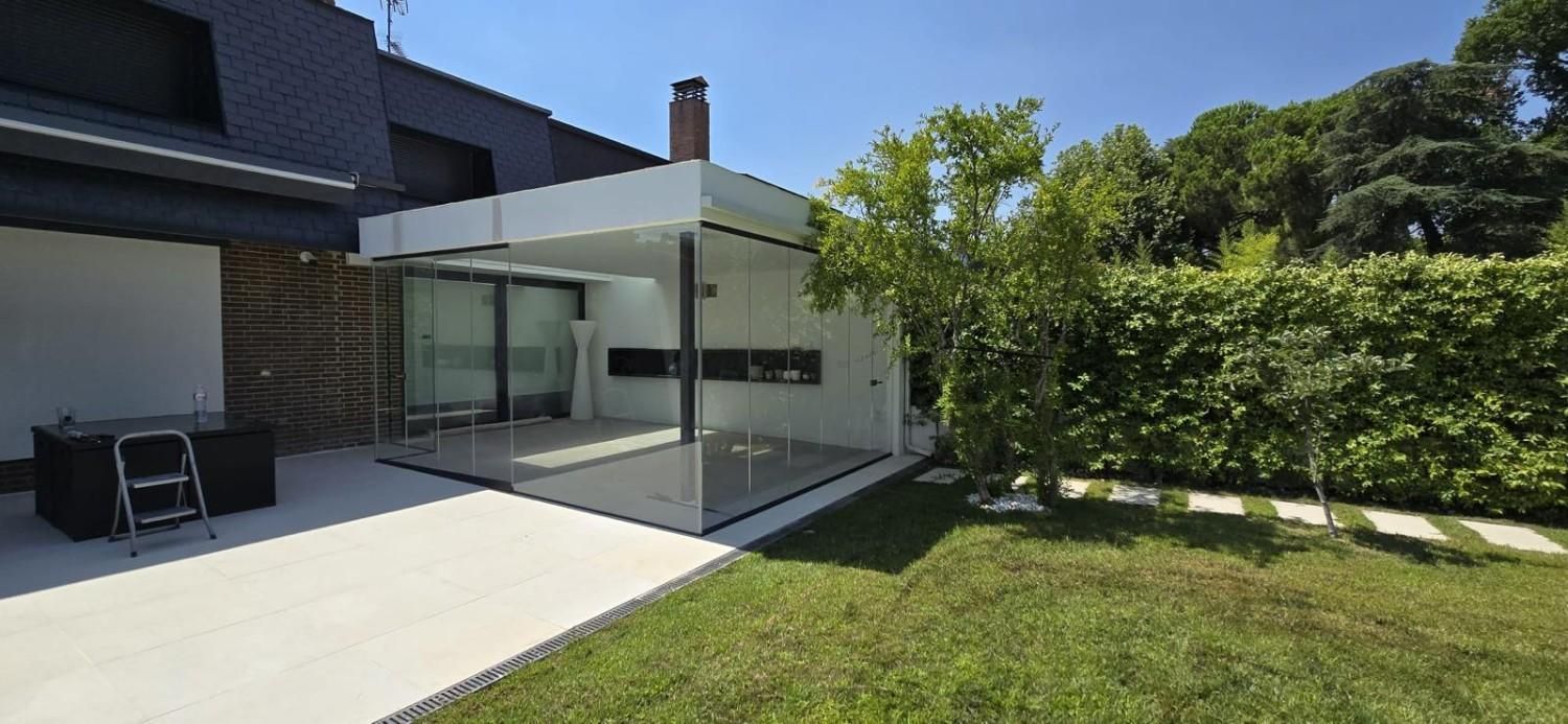 Patio de casa moderna con puertas corredizas de vidrio, pérgola blanca y césped verde junto a un seto.