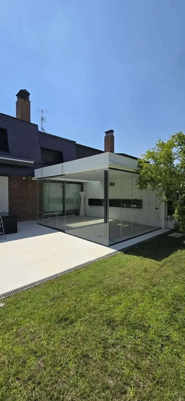 Ampliación de una casa moderna de color blanco con grandes puertas de cristal, patio y césped verde
