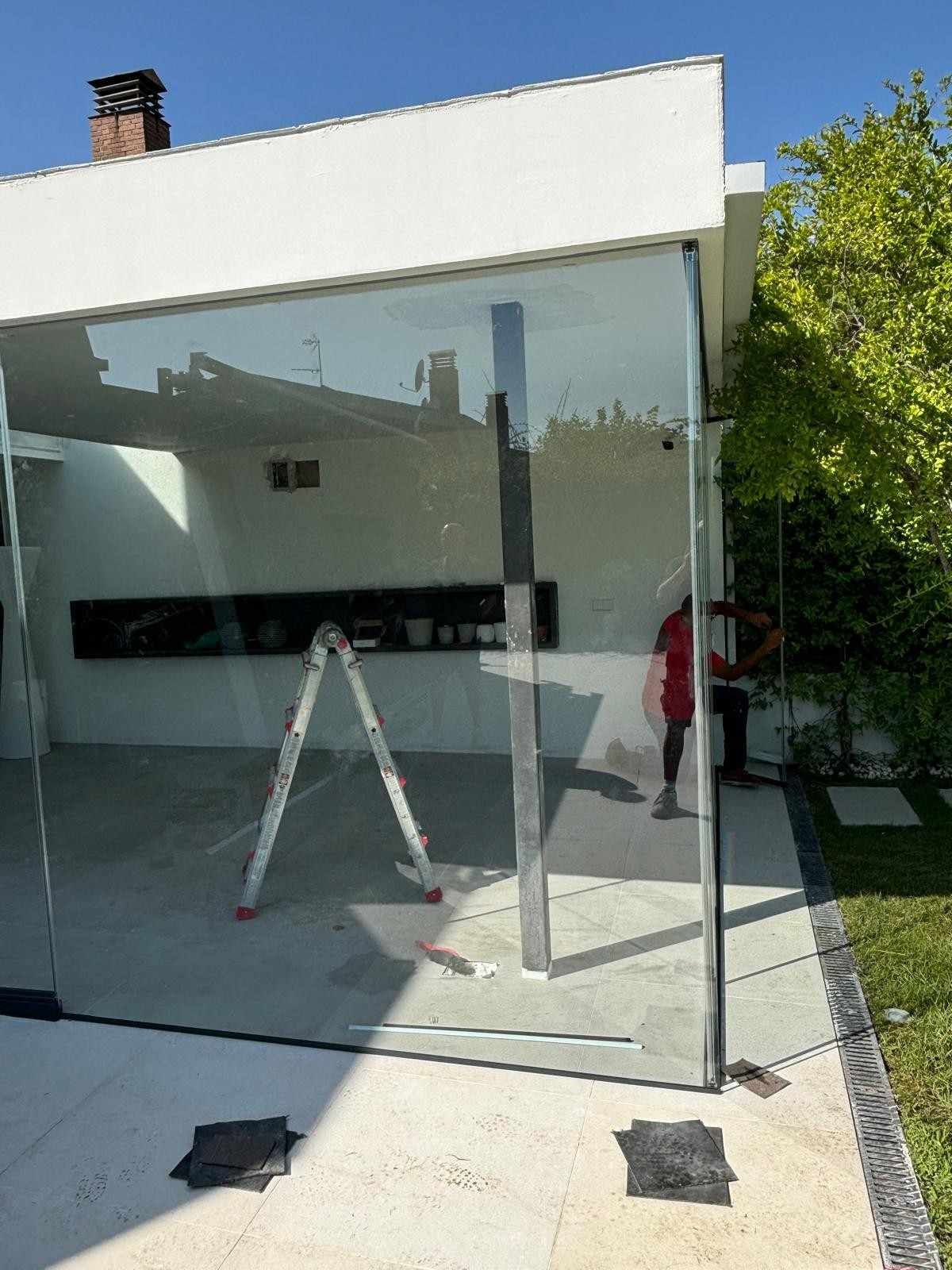 Un cerramiento de cristal en un patio con una escalera en el interior y una persona reflejada en la puerta