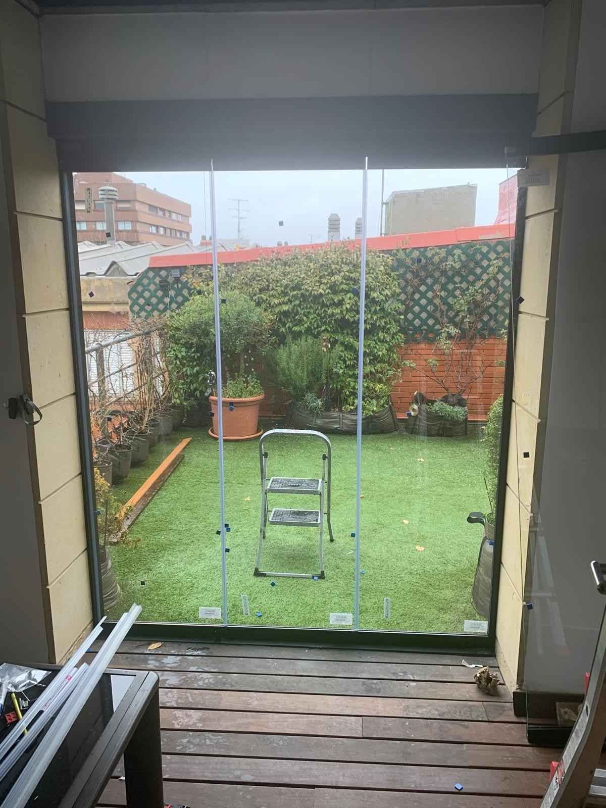 Vista a través de una puerta abierta a un pequeño patio trasero verde con una escalera y una planta en maceta, enmarcado