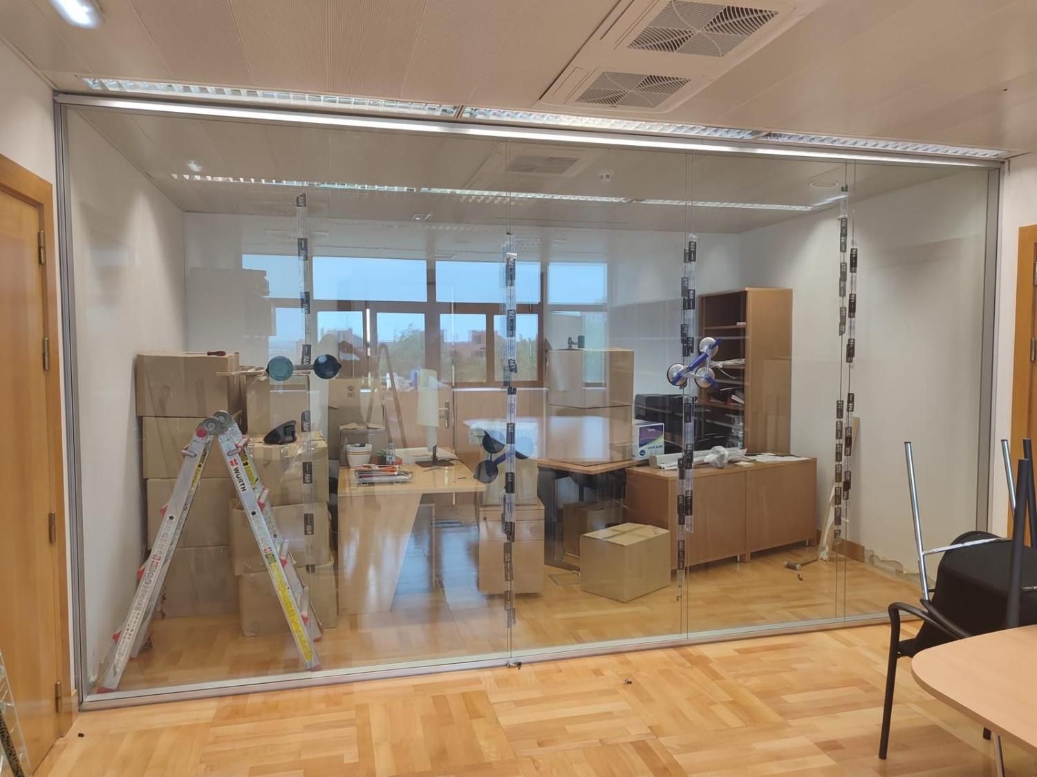 Oficina con una pared divisoria de plástico transparente, cajas de cartón y una escalera a la izquierda.