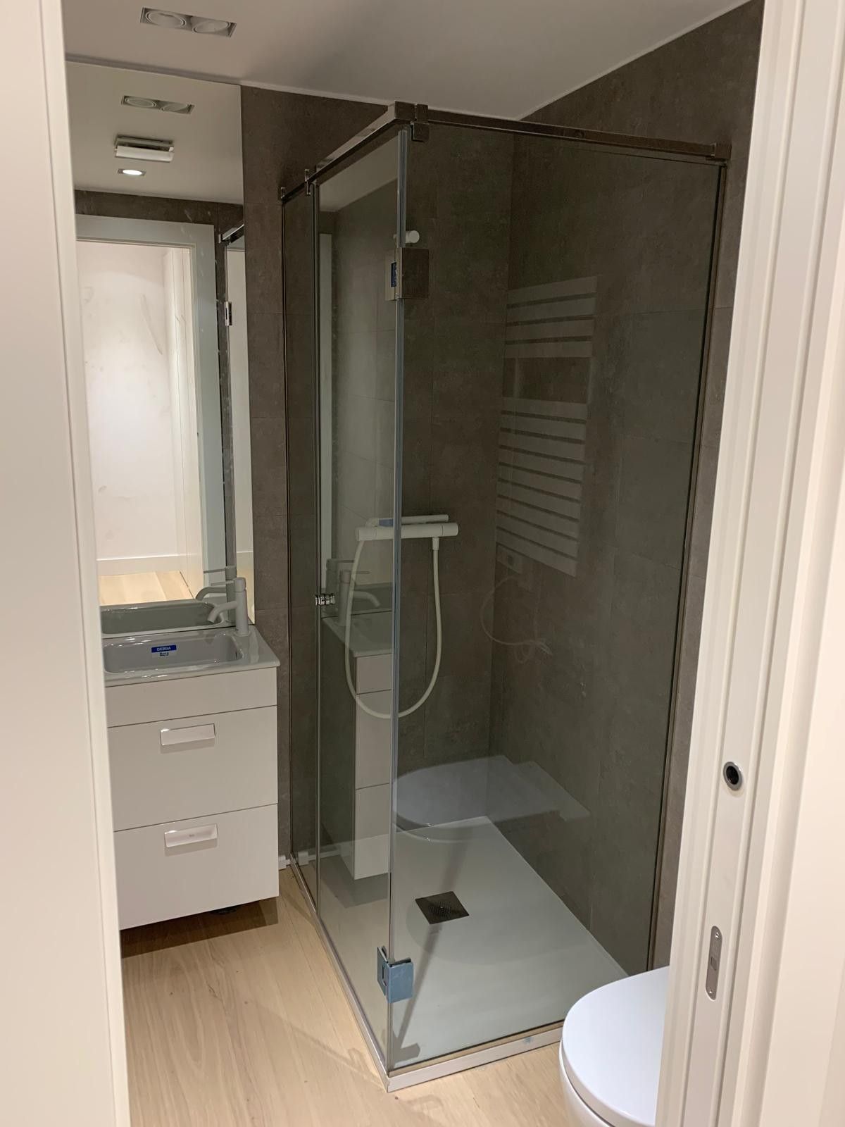 Baño moderno con cabina de ducha de cristal, lavabo y inodoro parcialmente visible.