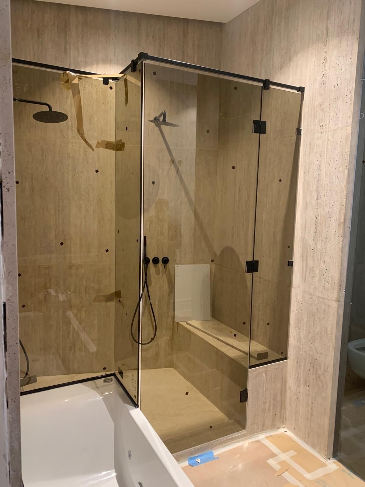 Baño moderno con ducha acristalada, paredes de azulejos beige, banco empotrado y borde de la bañera en primer plano.