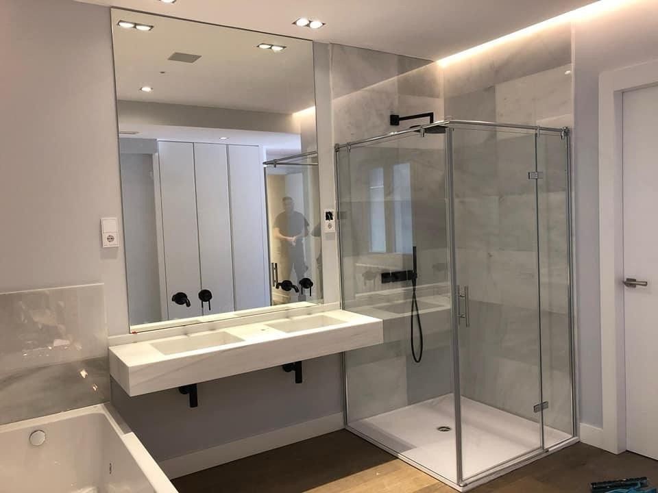 Baño moderno con lavabo suspendido, espejo grande y ducha con mampara de cristal.