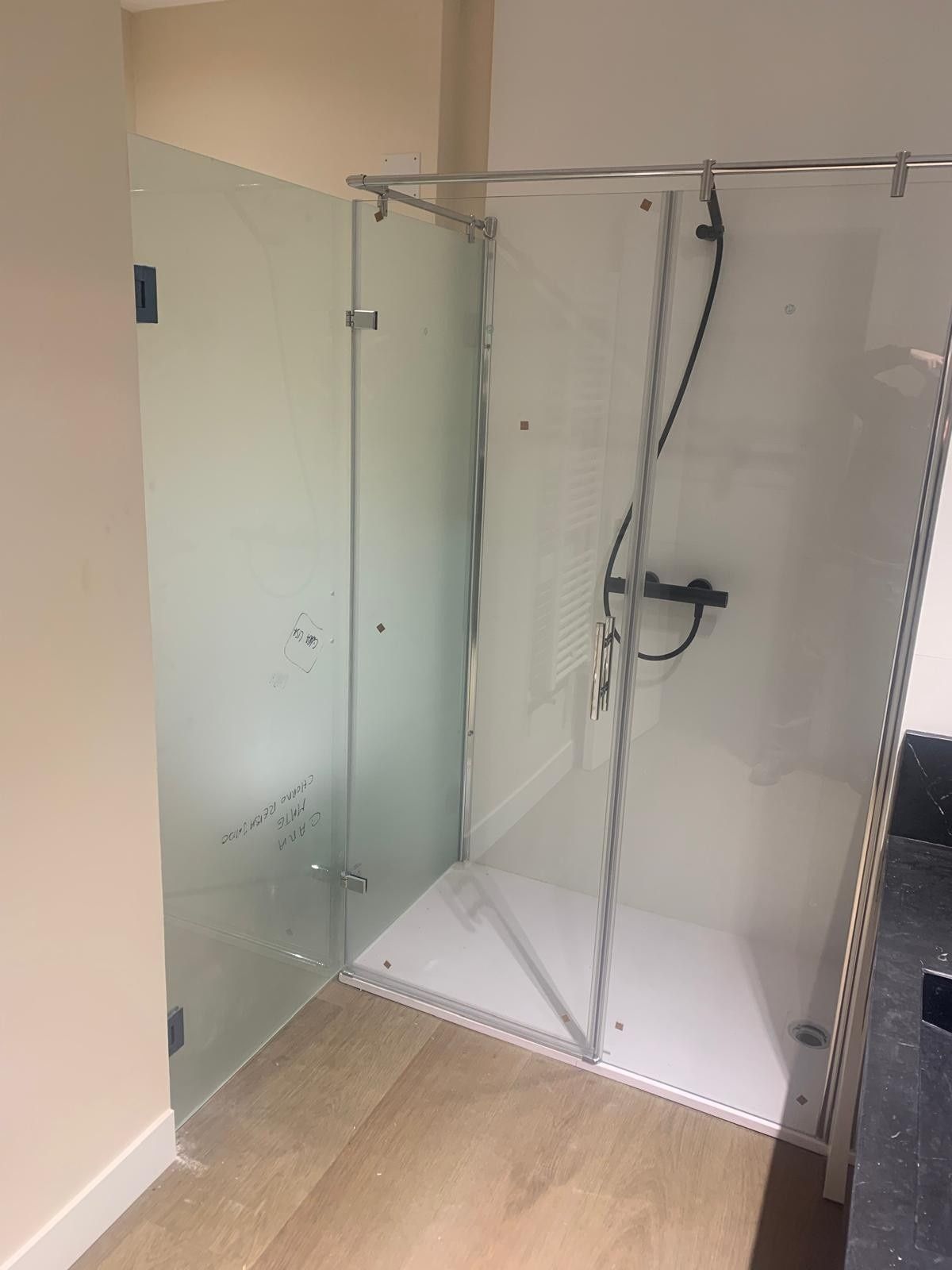 Mampara de ducha moderna de cristal con base blanca en un baño con suelo beige.