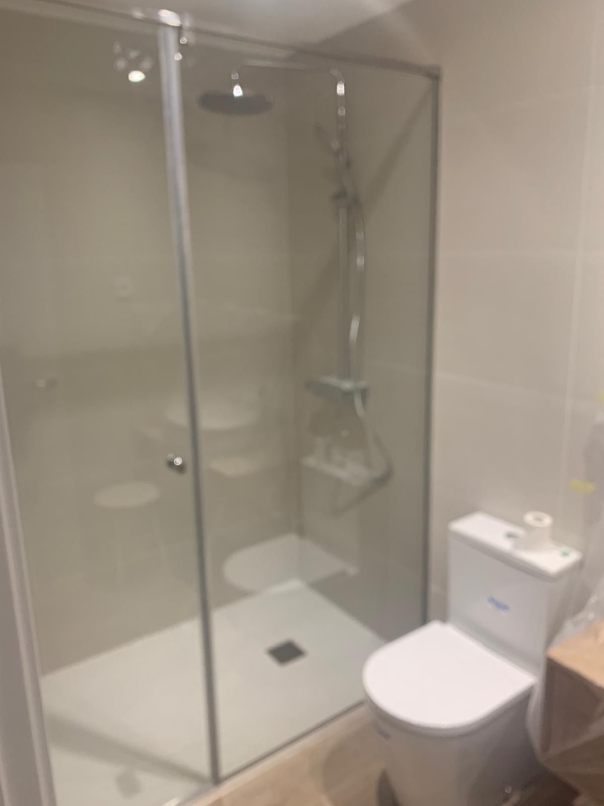 Baño pequeño y moderno con cabina de ducha de cristal, inodoro blanco y suelo de baldosas.