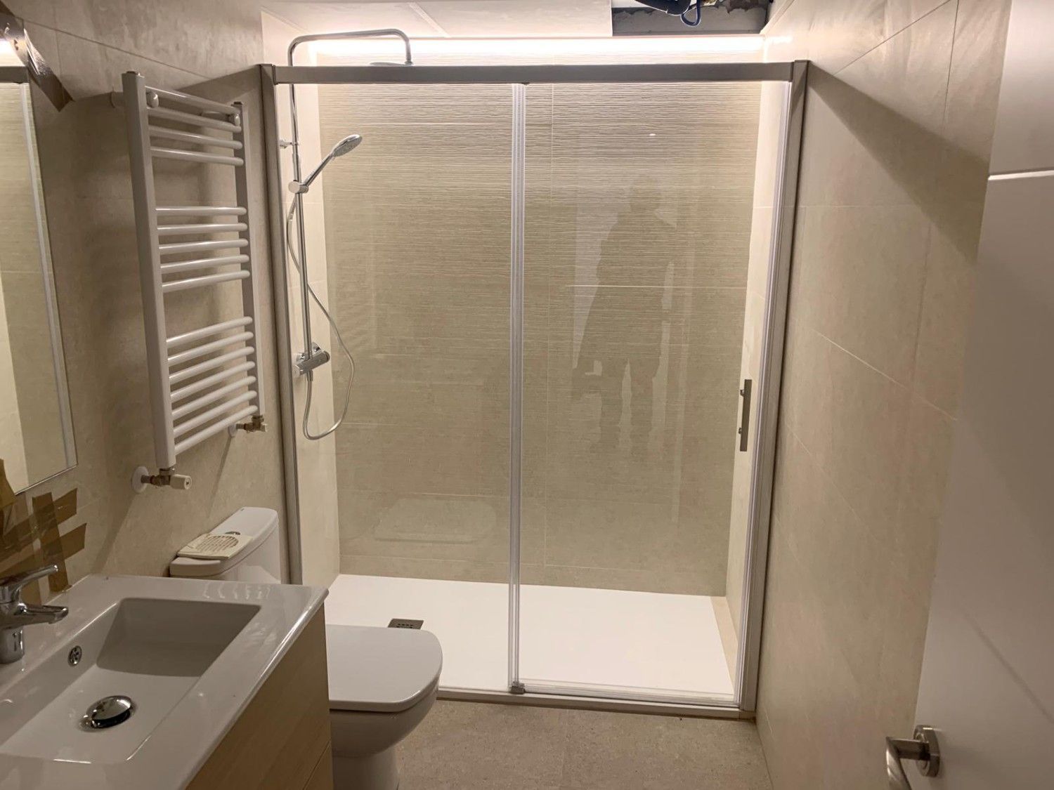 Baño accesible con ducha a ras de suelo, inodoro, lavabo y toallero plegable de pared.