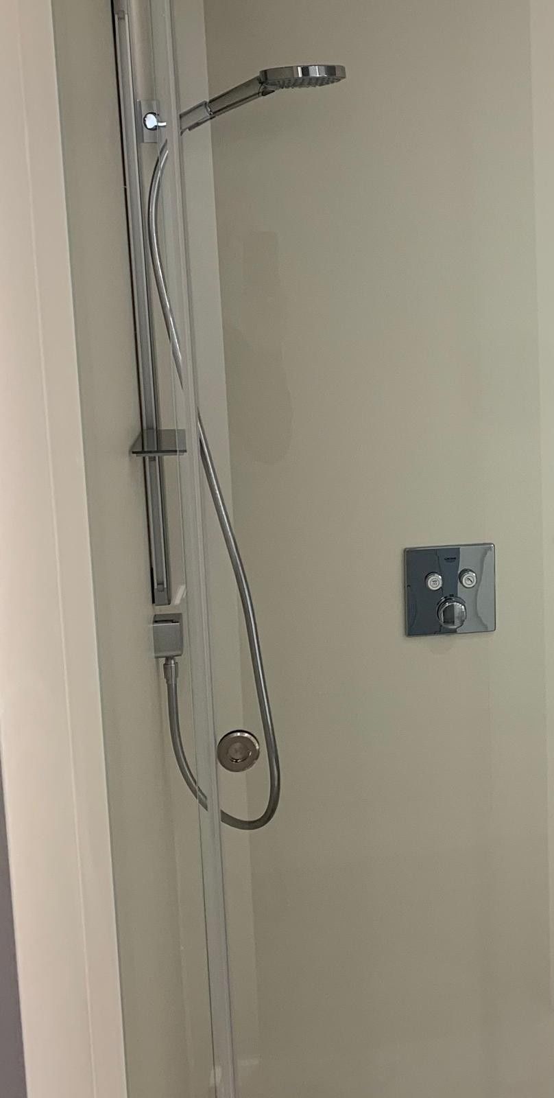 Manguera de ducha y cabezal de ducha de mano instalados en una pared beige del baño.