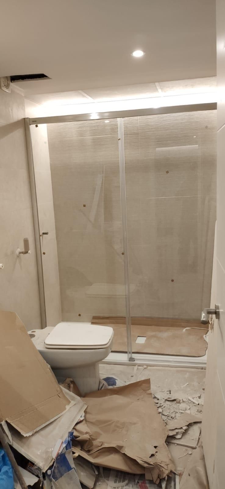 Baño en obras con inodoro, cabina de ducha, escombros y paredes sin terminar.