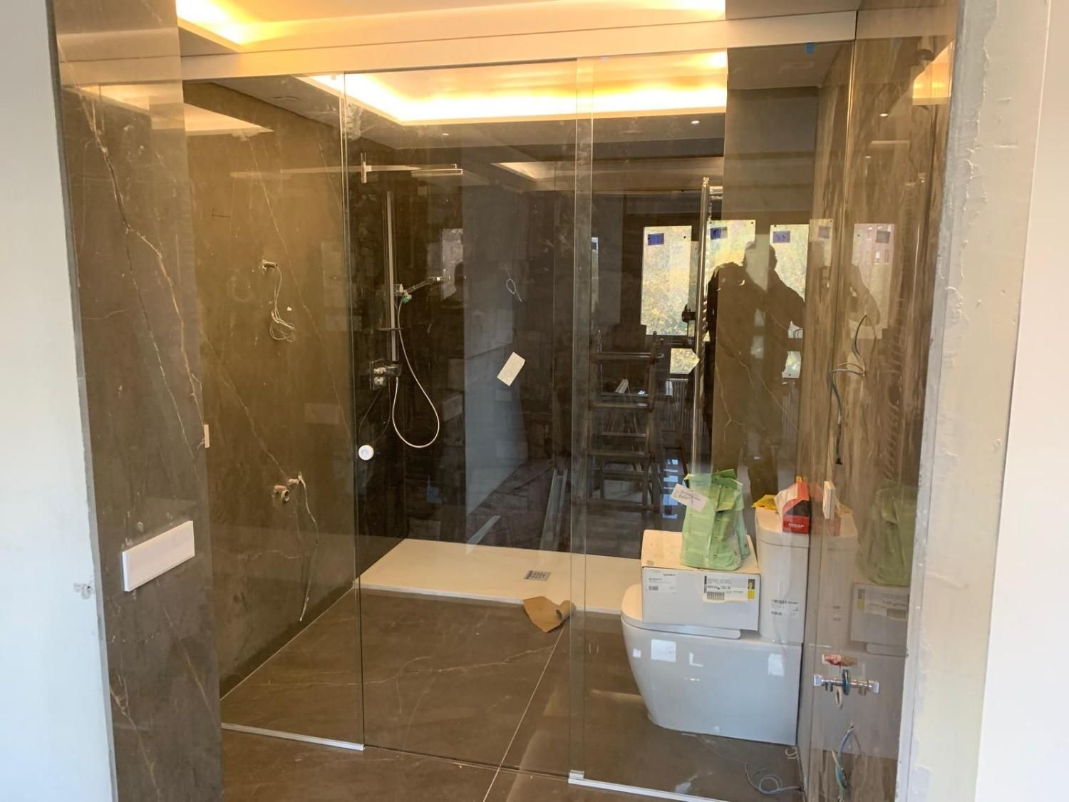 Baño moderno con paredes de mármol oscuro, cabina de ducha de cristal y tocador repleto de artículos de aseo personal.