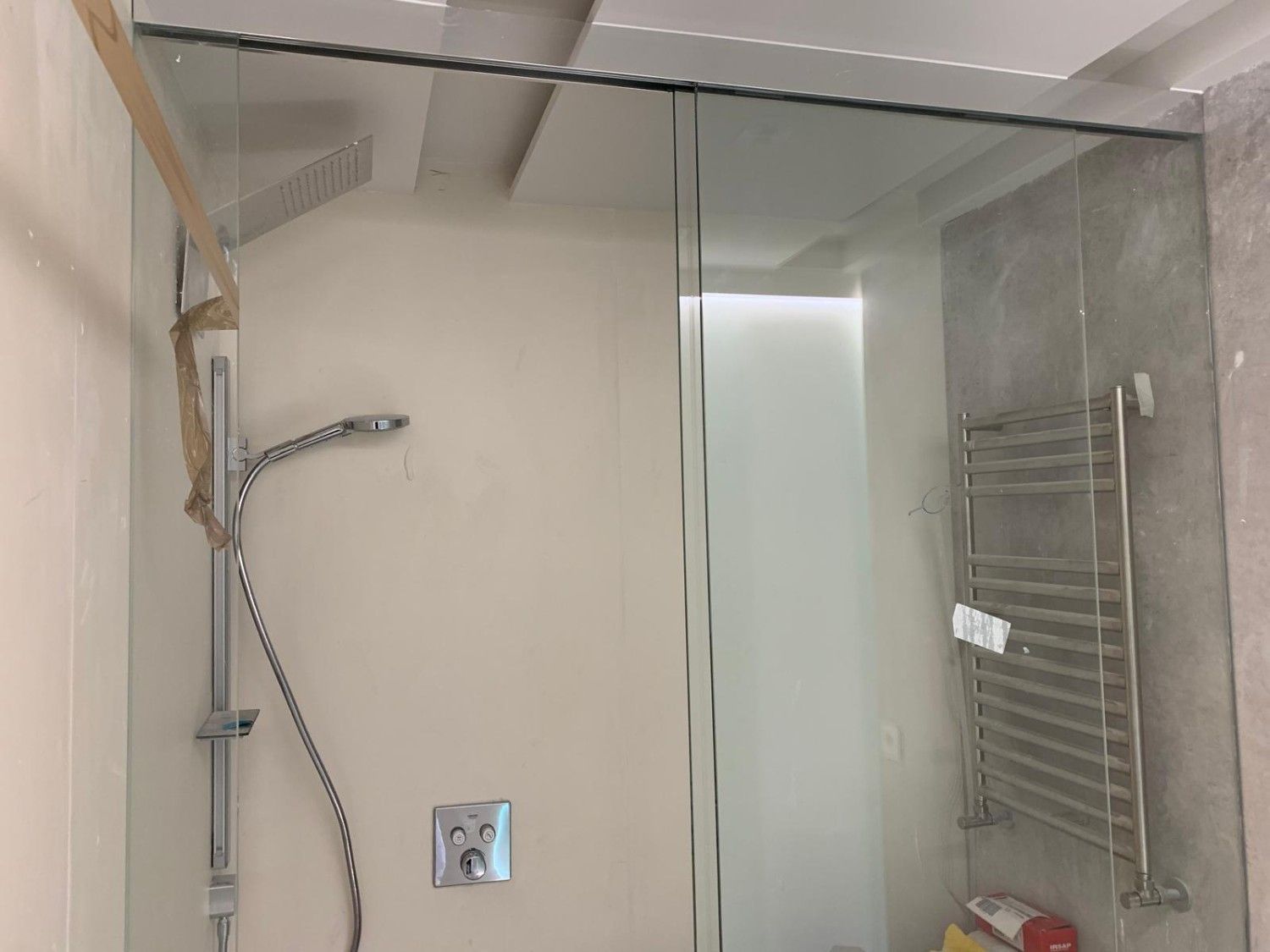 Mampara de ducha de cristal con grifería cromada, toallero eléctrico y paredes de baño de color beige.