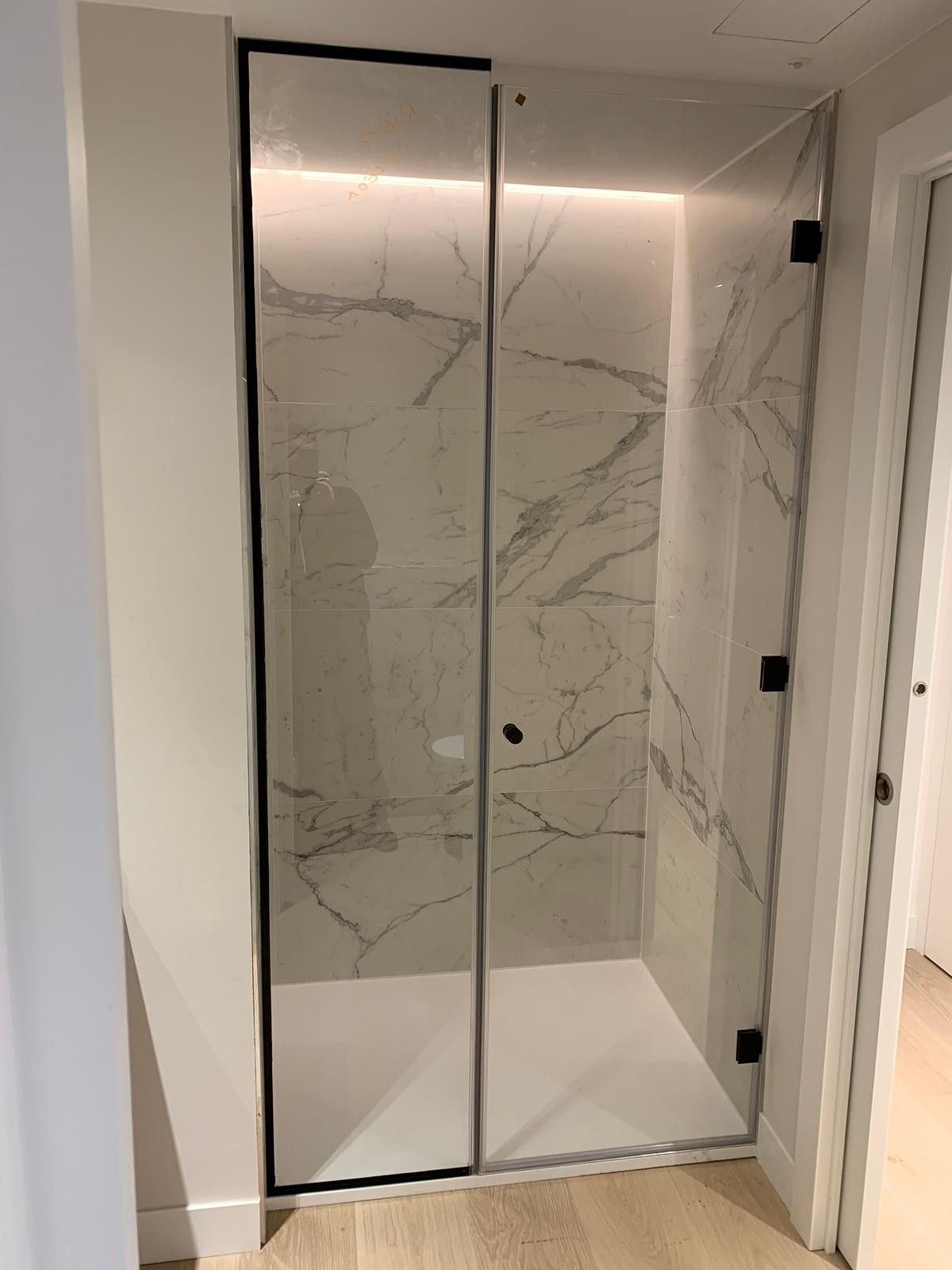 Mampara de ducha de cristal con paredes de azulejos de mármol y nicho de ducha empotrado con iluminación.