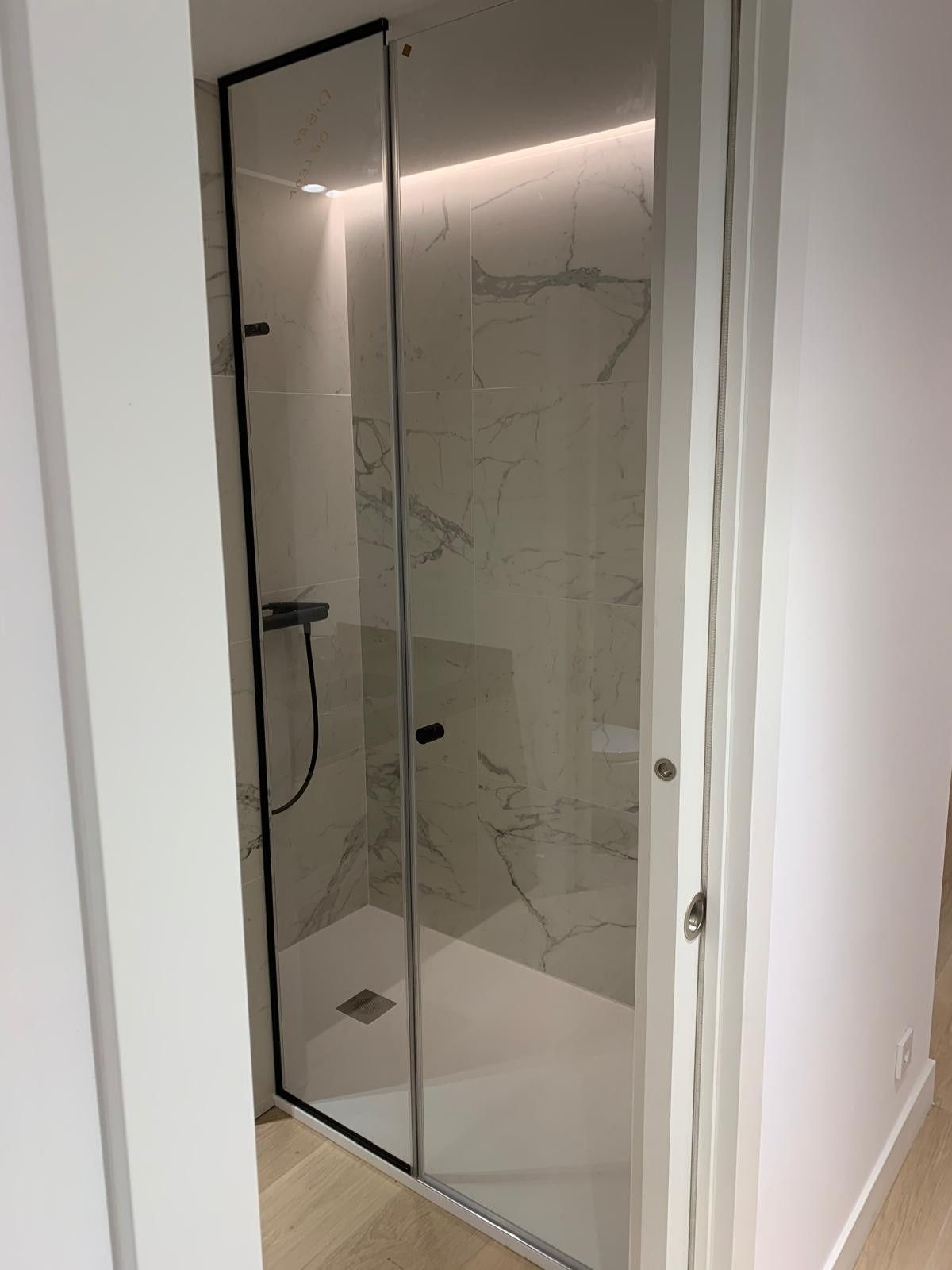 Mampara de ducha de cristal con marco negro en un baño blanco.