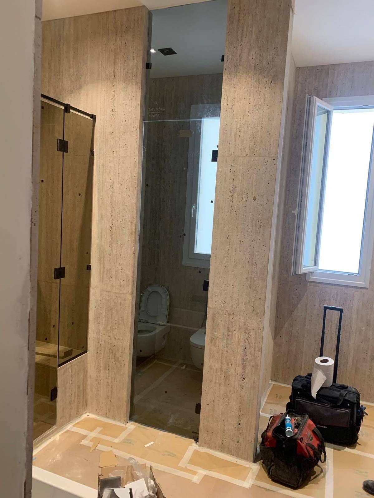 Pasillo en obras con paredes revestidas de madera, espejos, un inodoro a la vista y bolsas y herramientas en el suelo.