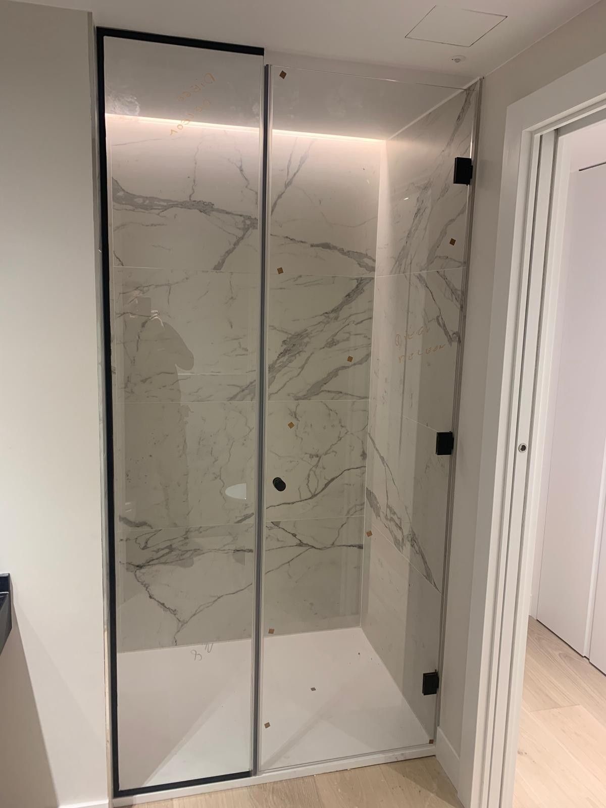 Baño moderno con ducha, paneles de pared con aspecto de mármol, puerta de cristal y suelo de baldosas blancas.