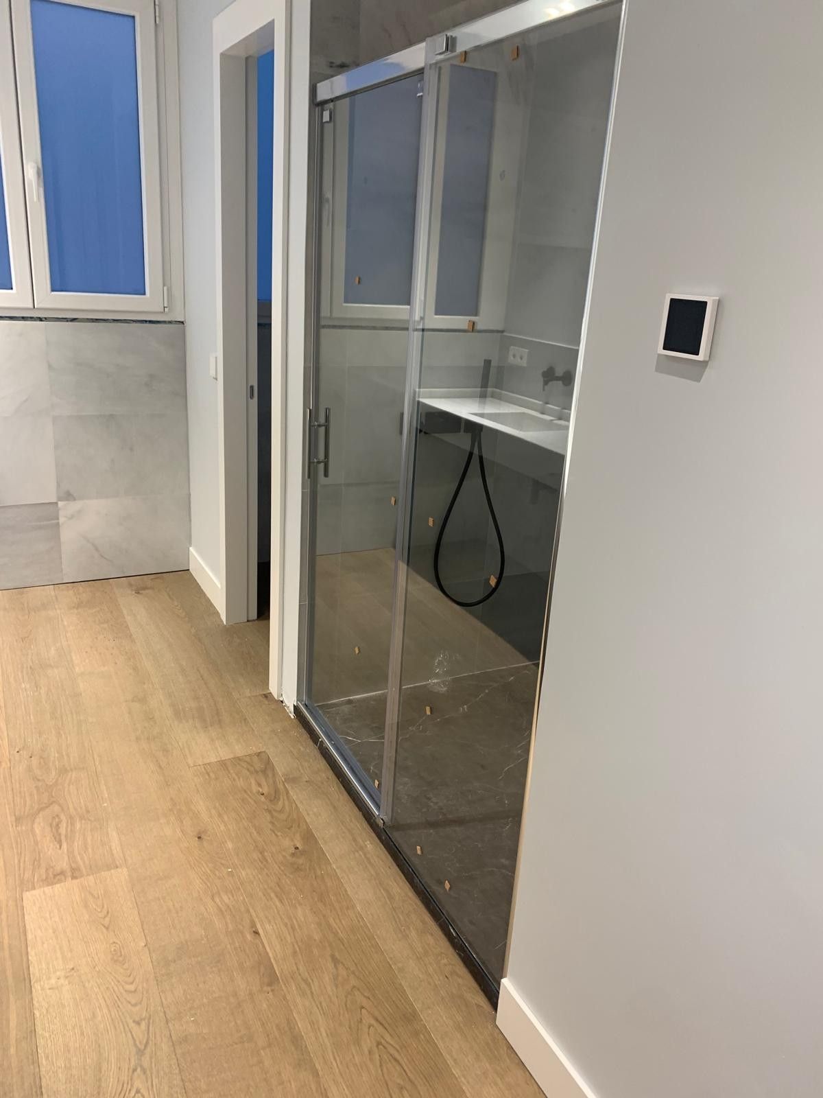 Puerta corredera de cristal en un pasillo de oficina moderno con suelo de madera clara y paredes grises.