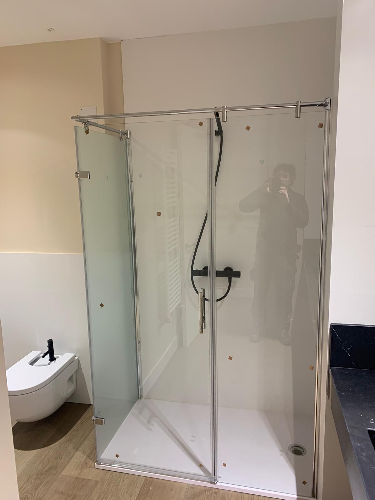 Mampara de ducha de cristal en un baño con azulejos beige y un inodoro blanco al lado.