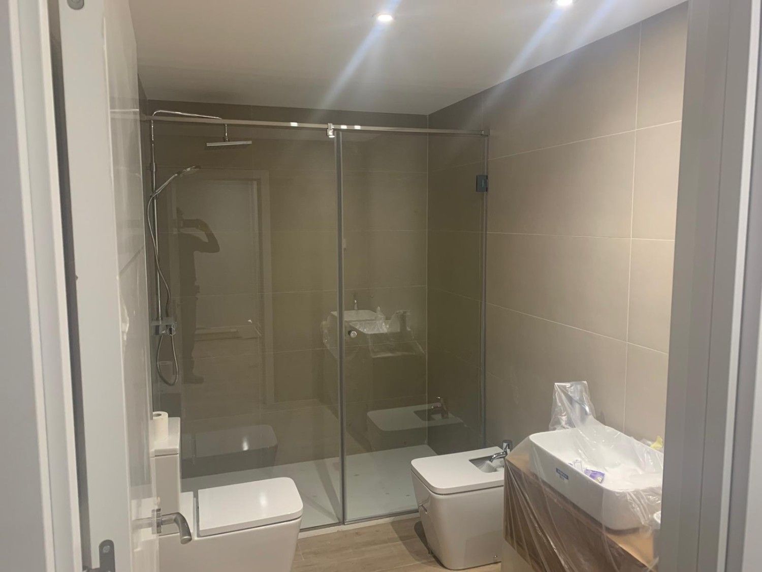 Baño moderno con ducha de cristal, inodoro y lavabo bajo iluminación cálida.