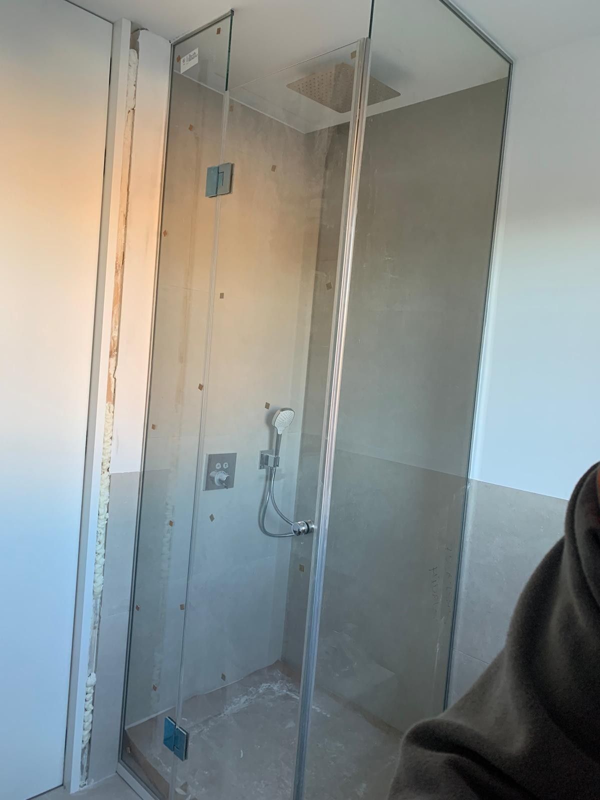 Ducha a ras de suelo en construcción con paneles de vidrio, paredes alicatadas y grifería visible.