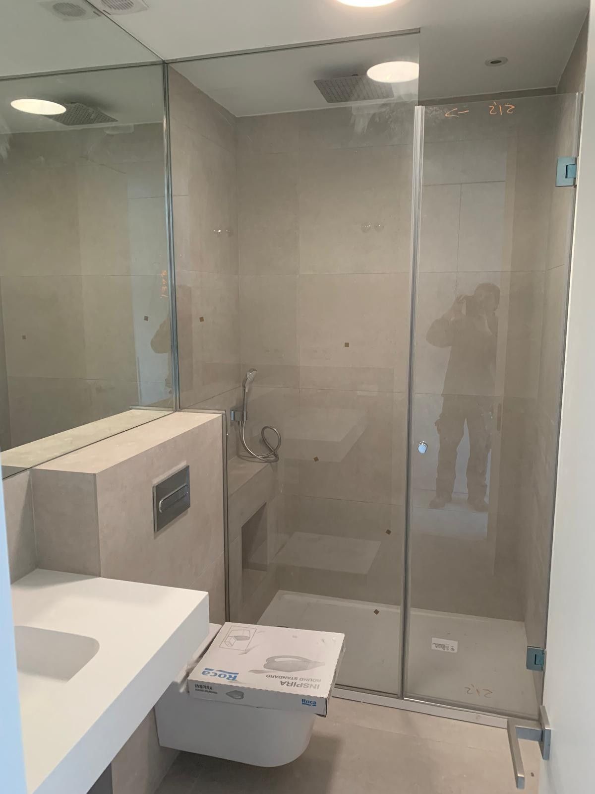 Baño moderno con ducha acristalada, inodoro y lavabo en una habitación con azulejos beige.