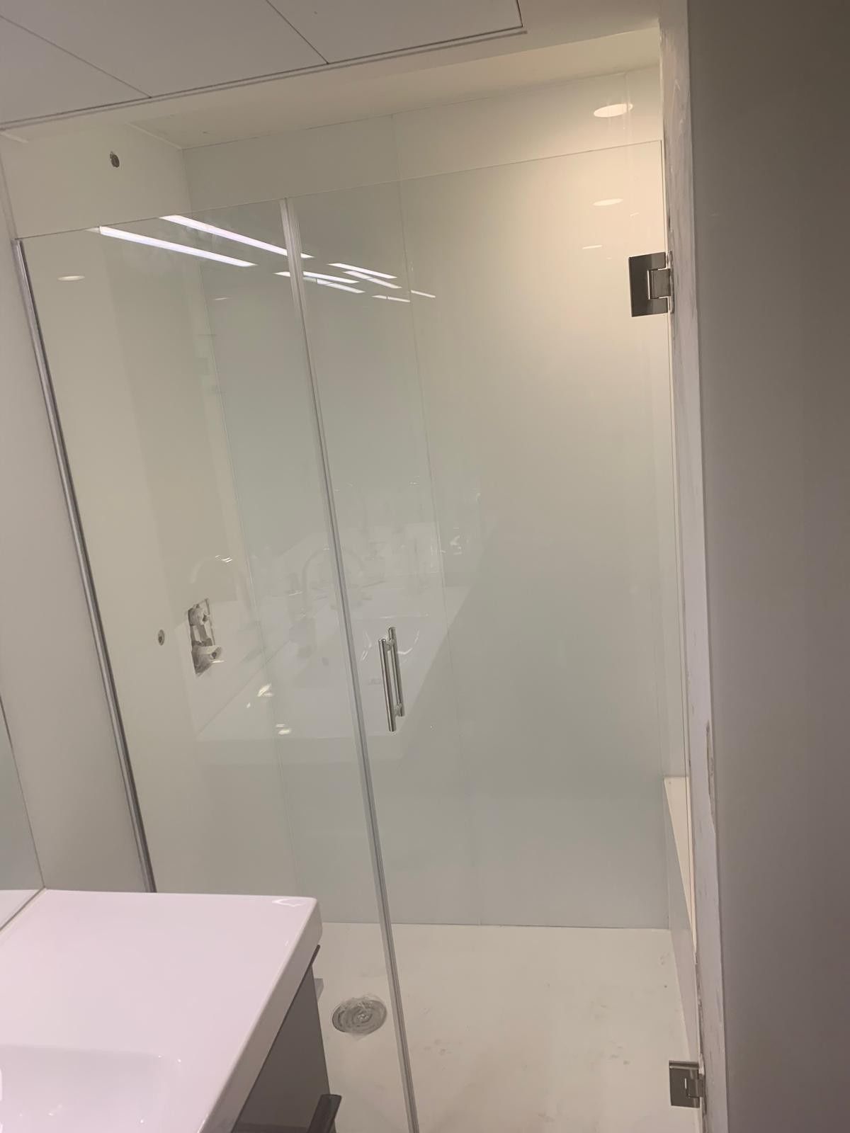 Mampara de ducha de cristal en un baño moderno con paredes blancas y un lavabo en primer plano.