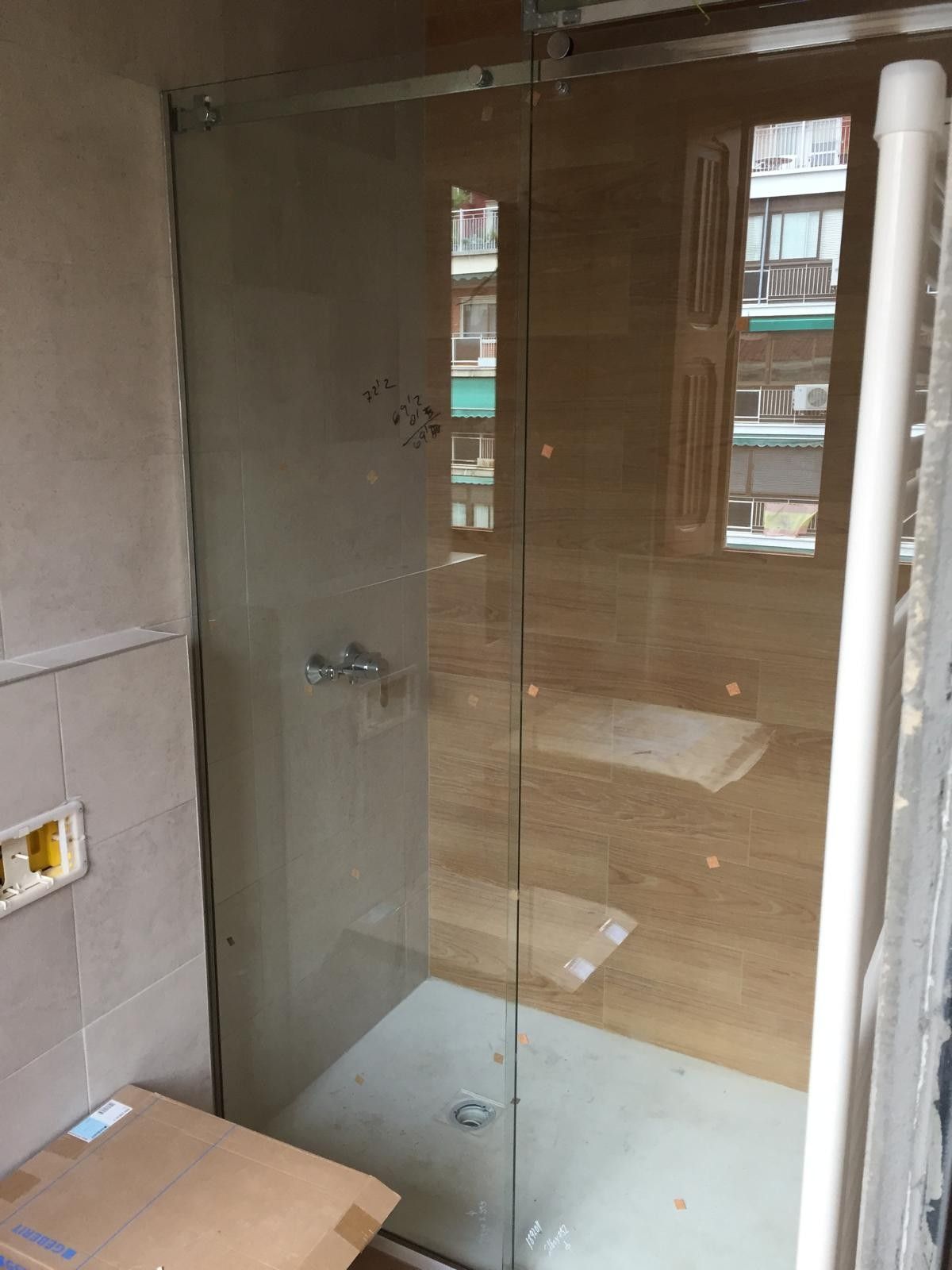 Baño pequeño con cabina de ducha de cristal, paredes alicatadas y una caja de cartón en el suelo.