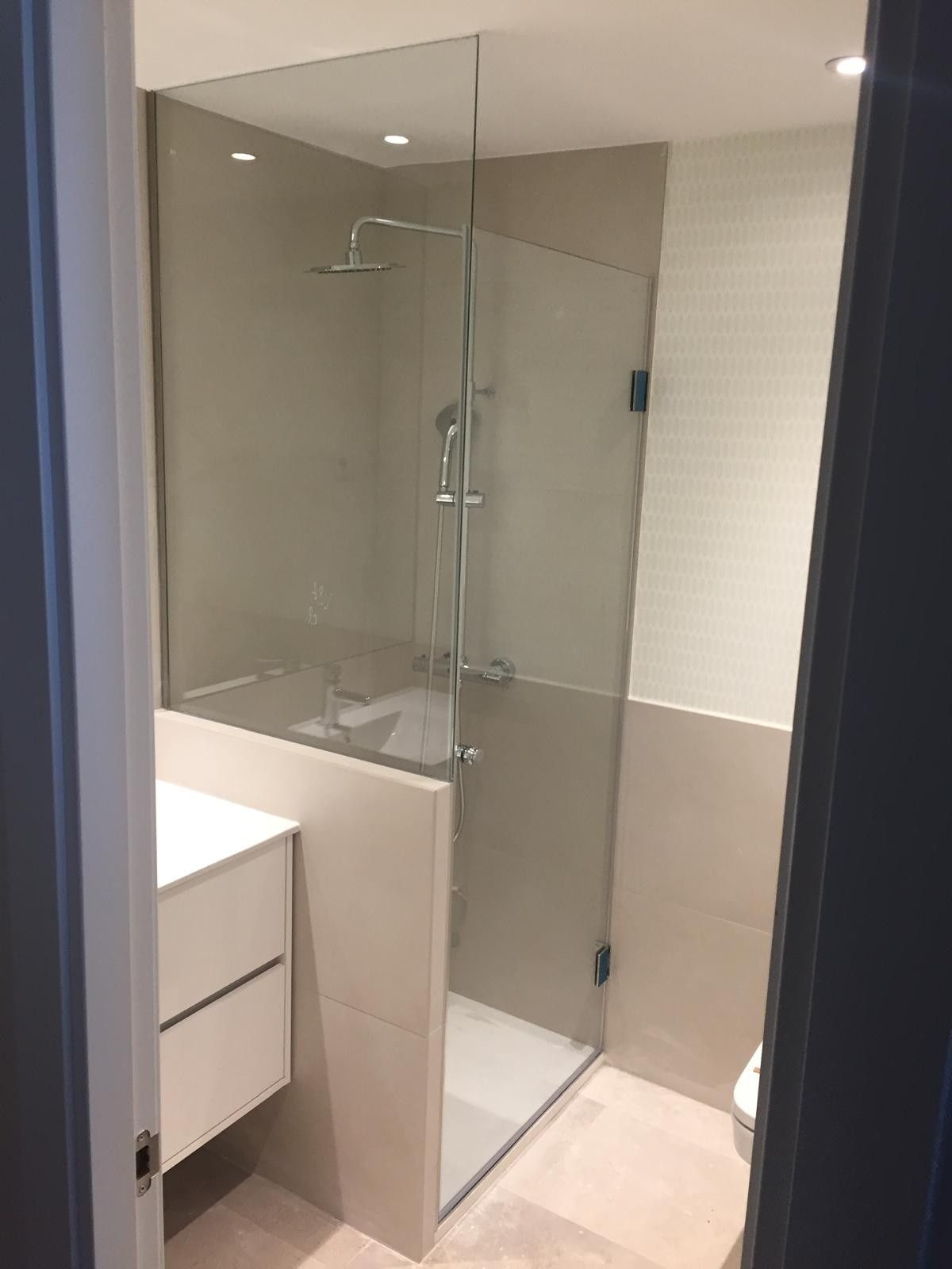 Baño moderno con cabina de ducha de cristal, azulejos beige y lavabo blanco.