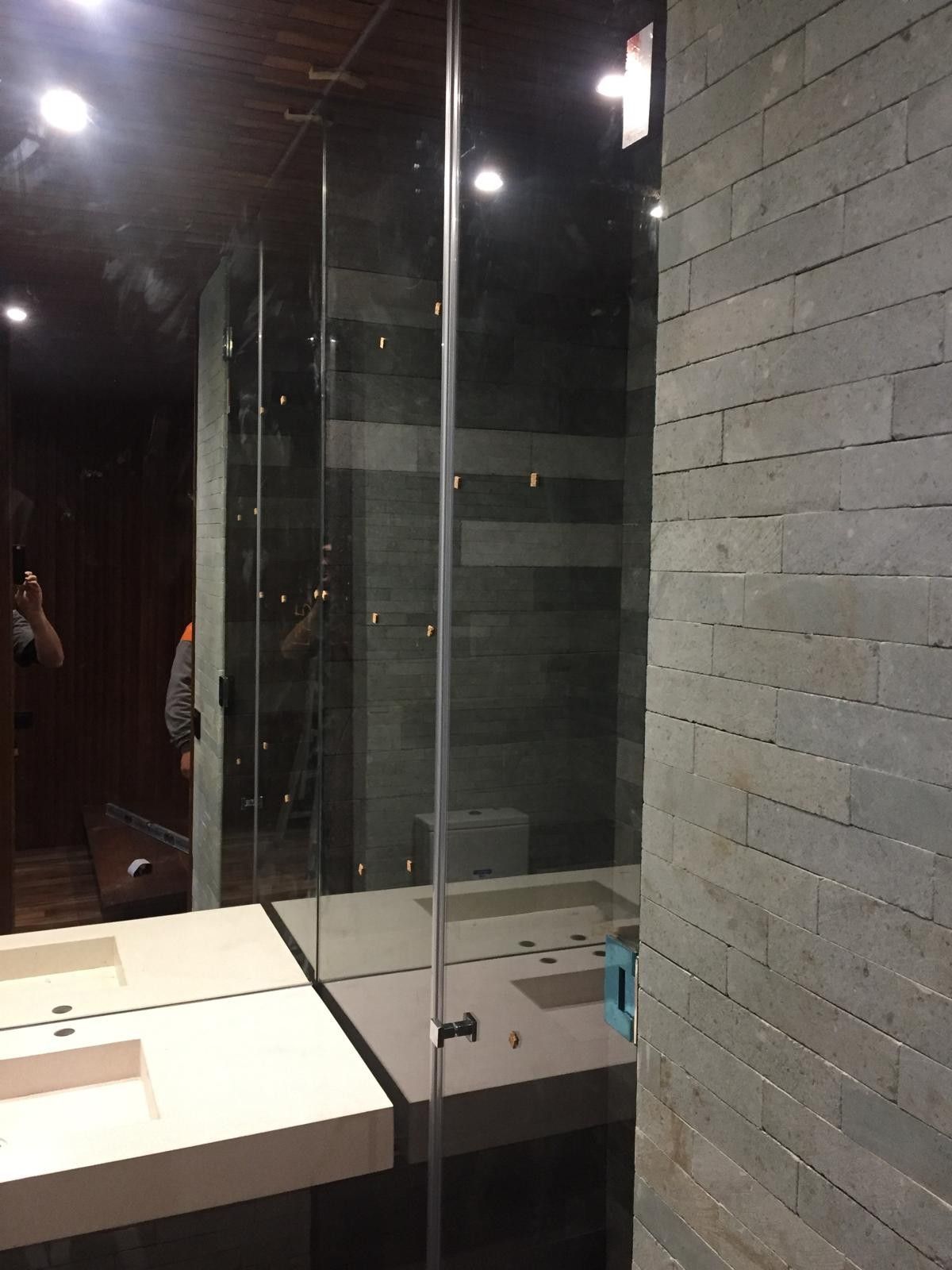 Baño con paredes de cristal, lavabos, espejos y paredes de azulejos grises por la noche.