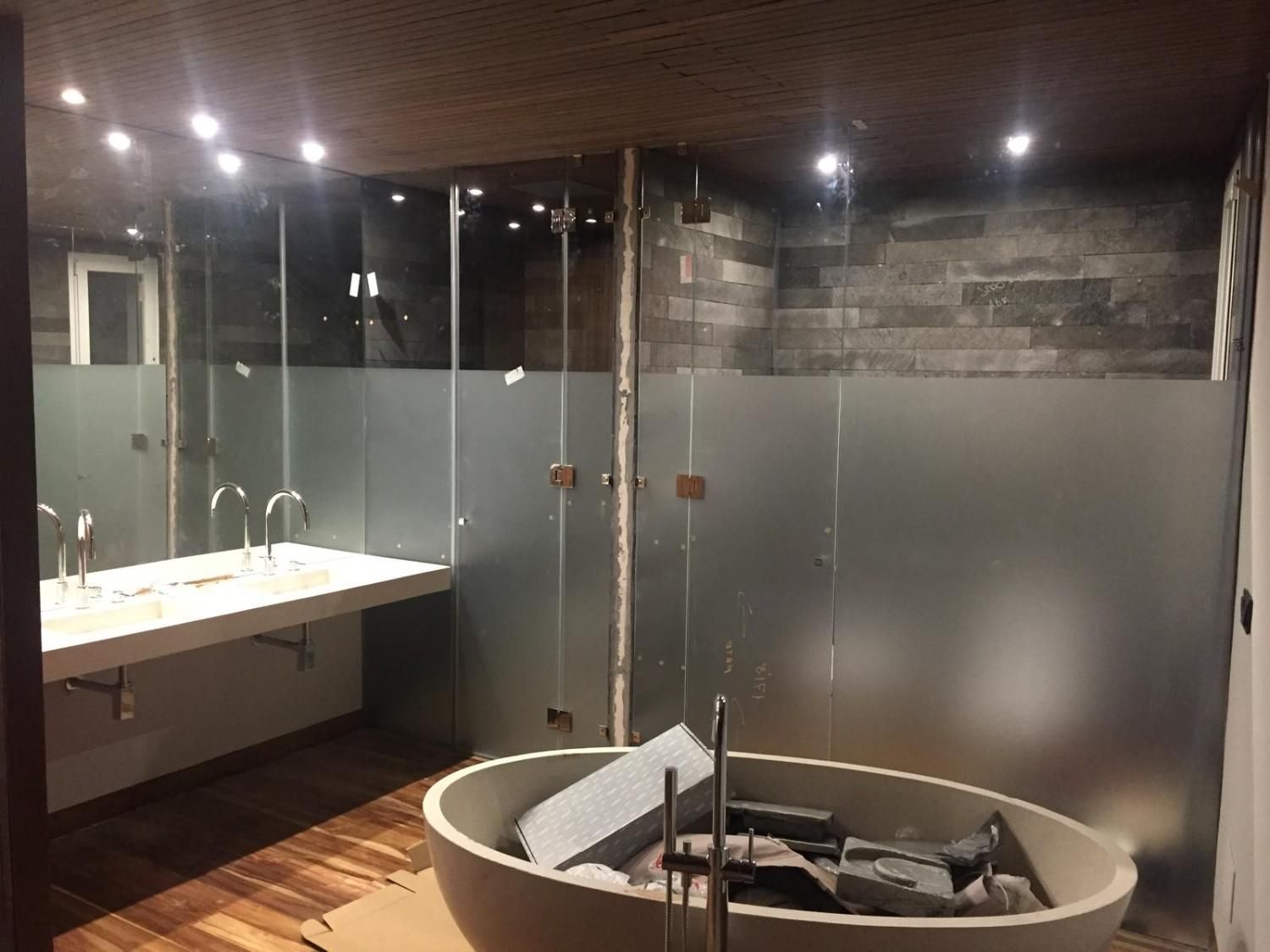 Baño moderno con ducha de cristal, tocador y bañera ovalada independiente en construcción con herramientas en el interior.