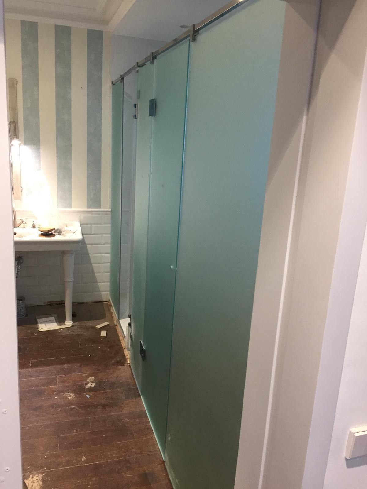 Habitación estrecha con papel pintado de rayas azules, puertas de color verde azulado y un pequeño escritorio