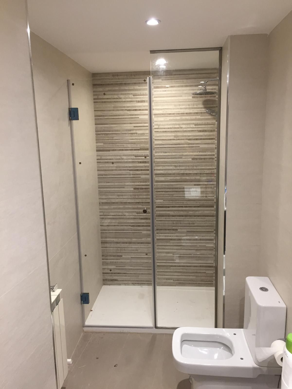 Baño moderno con ducha de cristal, paredes de azulejos beige y un inodoro blanco en primer plano.