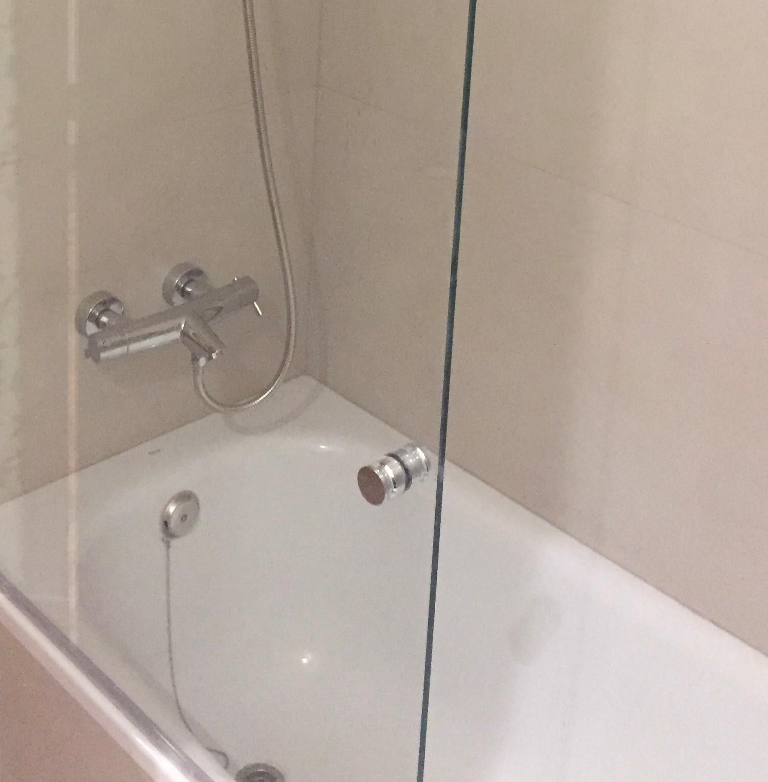 Bañera de esquina con grifo de ducha cromado y cabezal de ducha de mano detrás de un panel de vidrio.