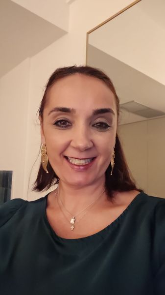Uma mulher usando óculos e uma camisa verde está sorrindo para a câmera.