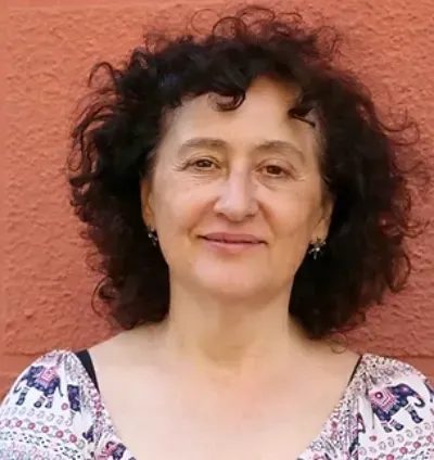 Retrato de una persona con cabello oscuro y rizado sonriendo contra una pared de coral texturizada.