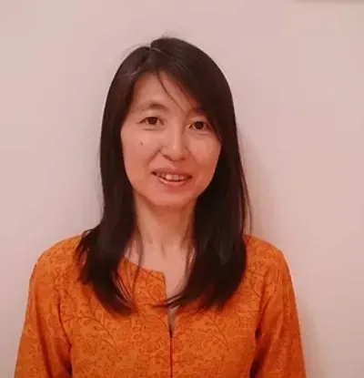 Mujer con blusa naranja sonriendo sobre un fondo liso de color claro.