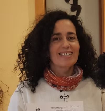 Persona sonriente con cabello oscuro y rizado, sosteniendo un certificado, vestida con una blusa blanca
