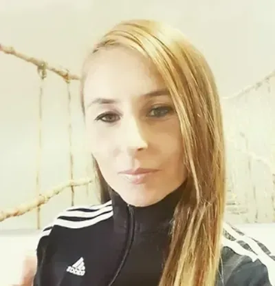 Retrato de una mujer con una chaqueta Adidas negra contra una pared de ladrillo claro.