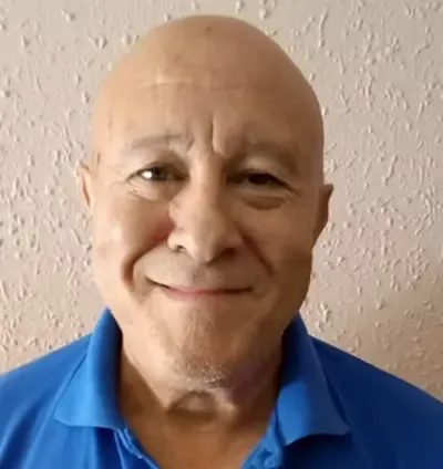 Hombre calvo sonriente con una camisa polo azul contra una pared texturizada.
