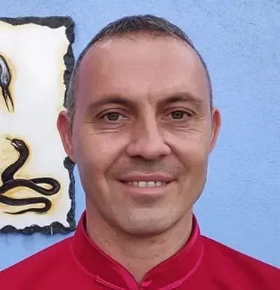 Una persona con una blusa roja sonríe frente a una pared azul con una obra de arte al fondo.
