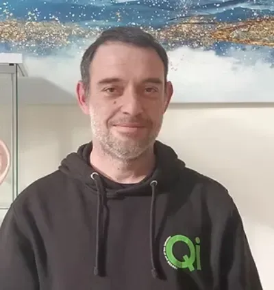Hombre sonriente con una sudadera negra con el logo verde de Qi, de pie en el interior de un edificio