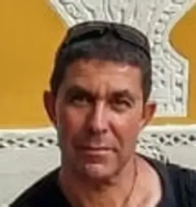 Retrato de un hombre con camisa negra contra una pared amarilla y blanca.