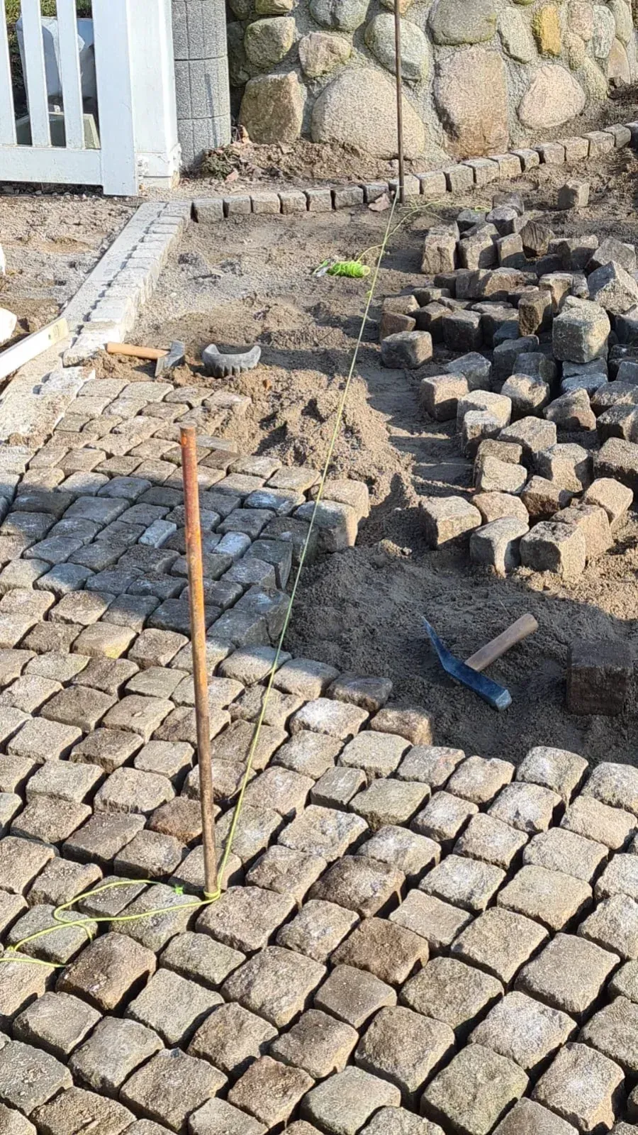 Kopfsteinpflasterweg im Bau; braune Steinblöcke, Erde und Werkzeuge liegen verstreut herum.