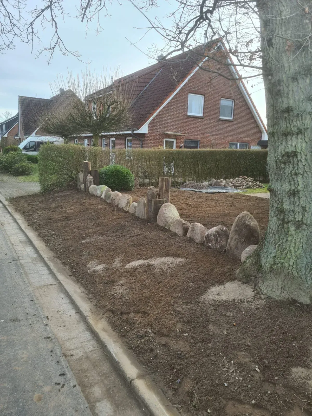 Ein Haus mit rotem Dach und einem neu angelegten, mit Steinen eingefassten Gartenbeet.