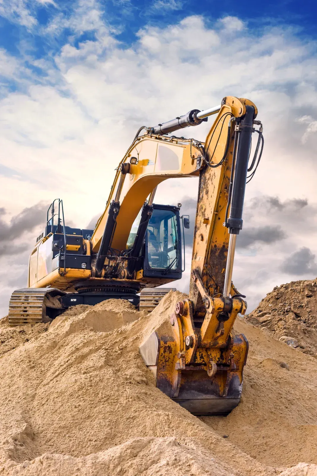 Gelber Bagger auf einem Sandhaufen vor bewölktem Himmel.