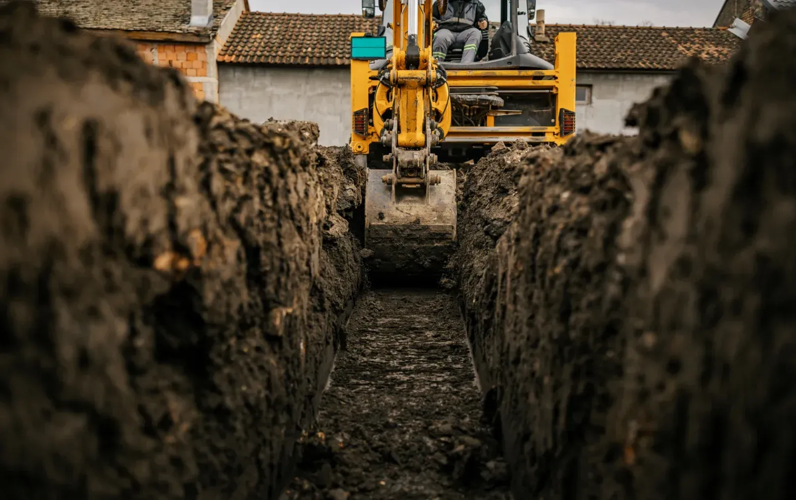 Ein gelber Bagger gräbt einen langen Graben in die Erde – eine Baustelle.
