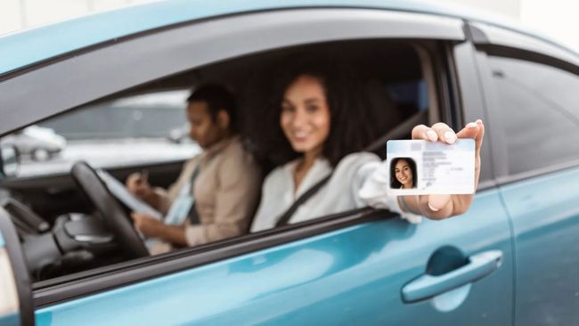 Una mujer está sentada en un coche sosteniendo un permiso de conducir.