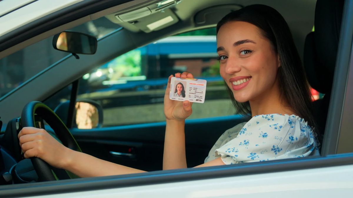 Una mujer está sentada en un coche sosteniendo un permiso de conducir.