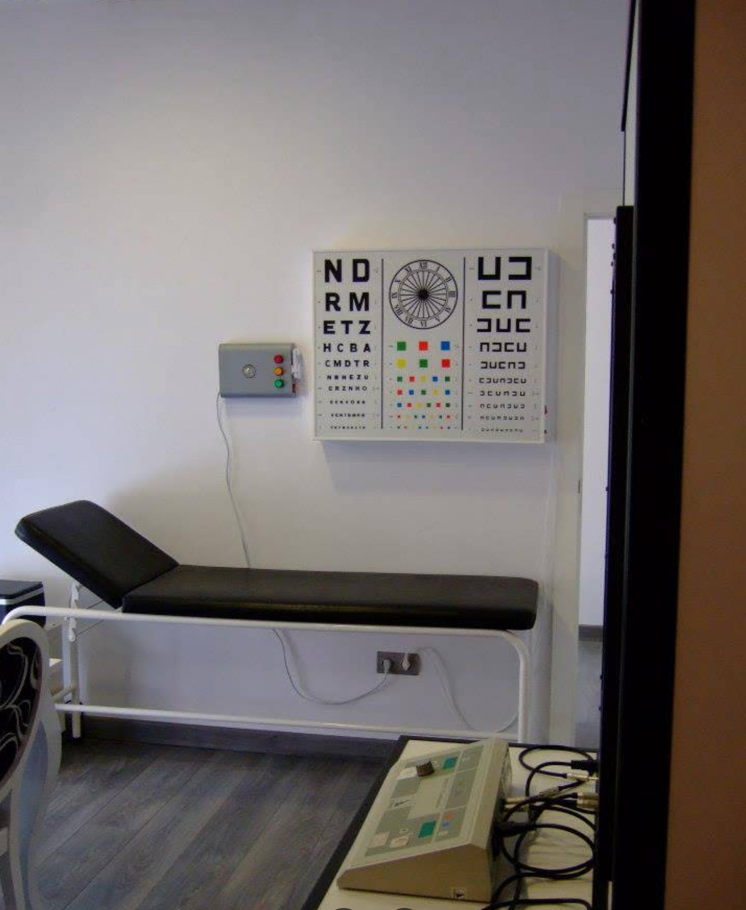Un consultorio médico con una cama y una tabla optométrica en la pared.