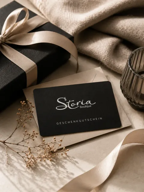 Schwarze Geschenkbox mit beigefarbenem Band und Satinstoff auf neutralem Tisch, daneben eine Visitenkarte mit der Aufschrift „Storia“.